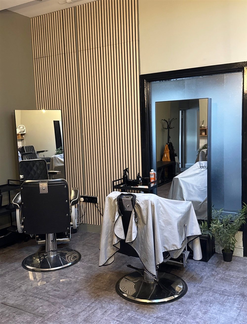 Two barber chairs in front of a slatted wooden feature wall
